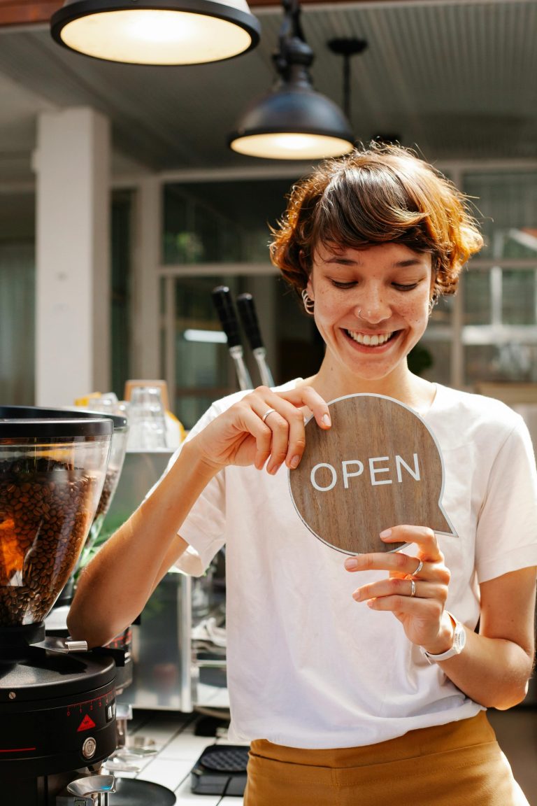 Smiling local business owner holding an open sign in her cafe
